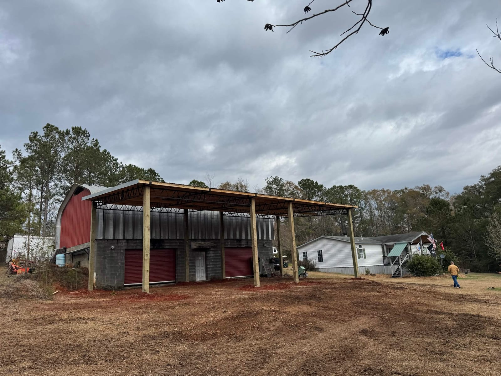 Pole barn cover extension built alongside an existing red barn with roll-up doors