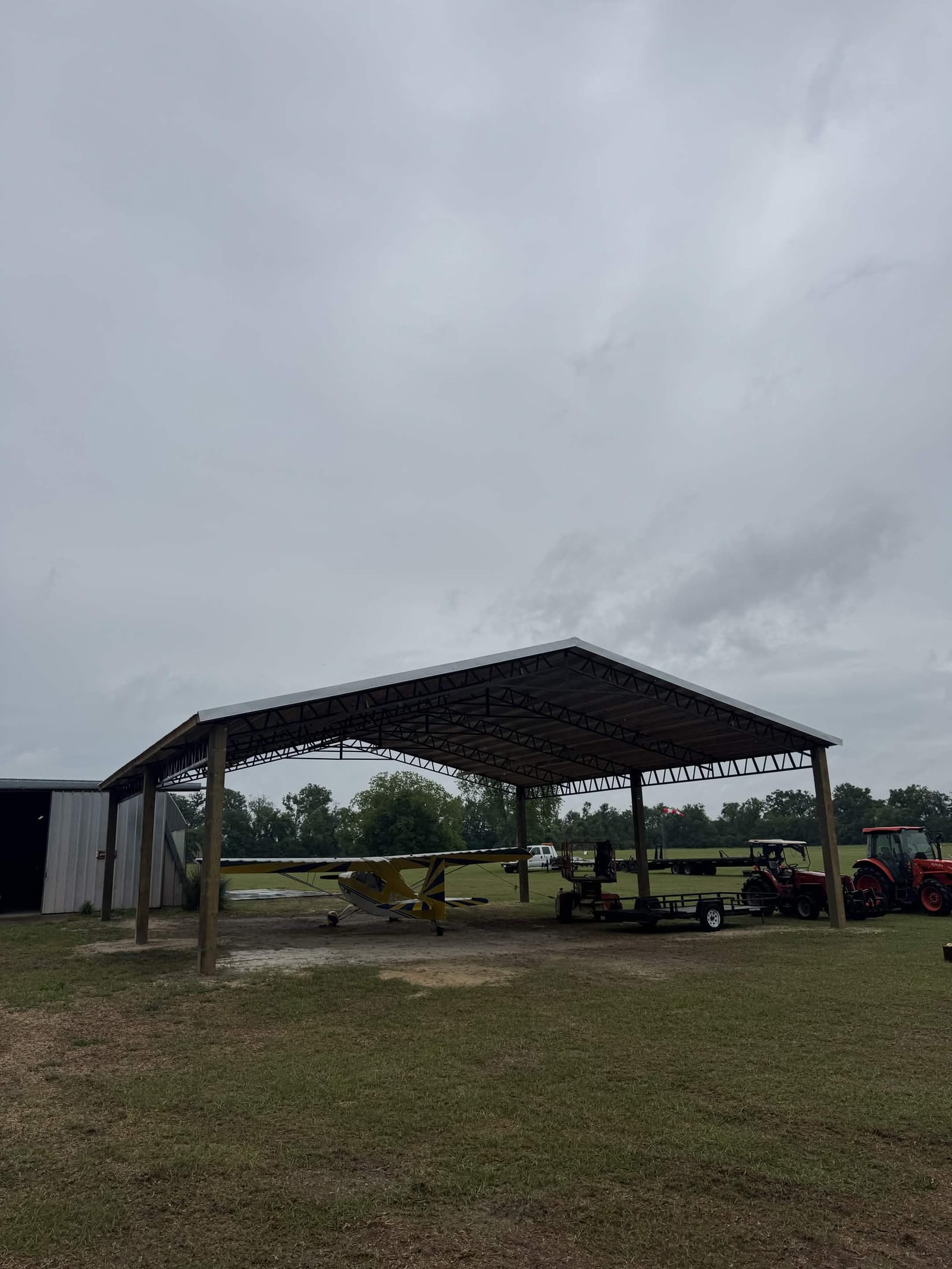 Pole barn sheltering a small aircraft and tractor on a rural airstrip property